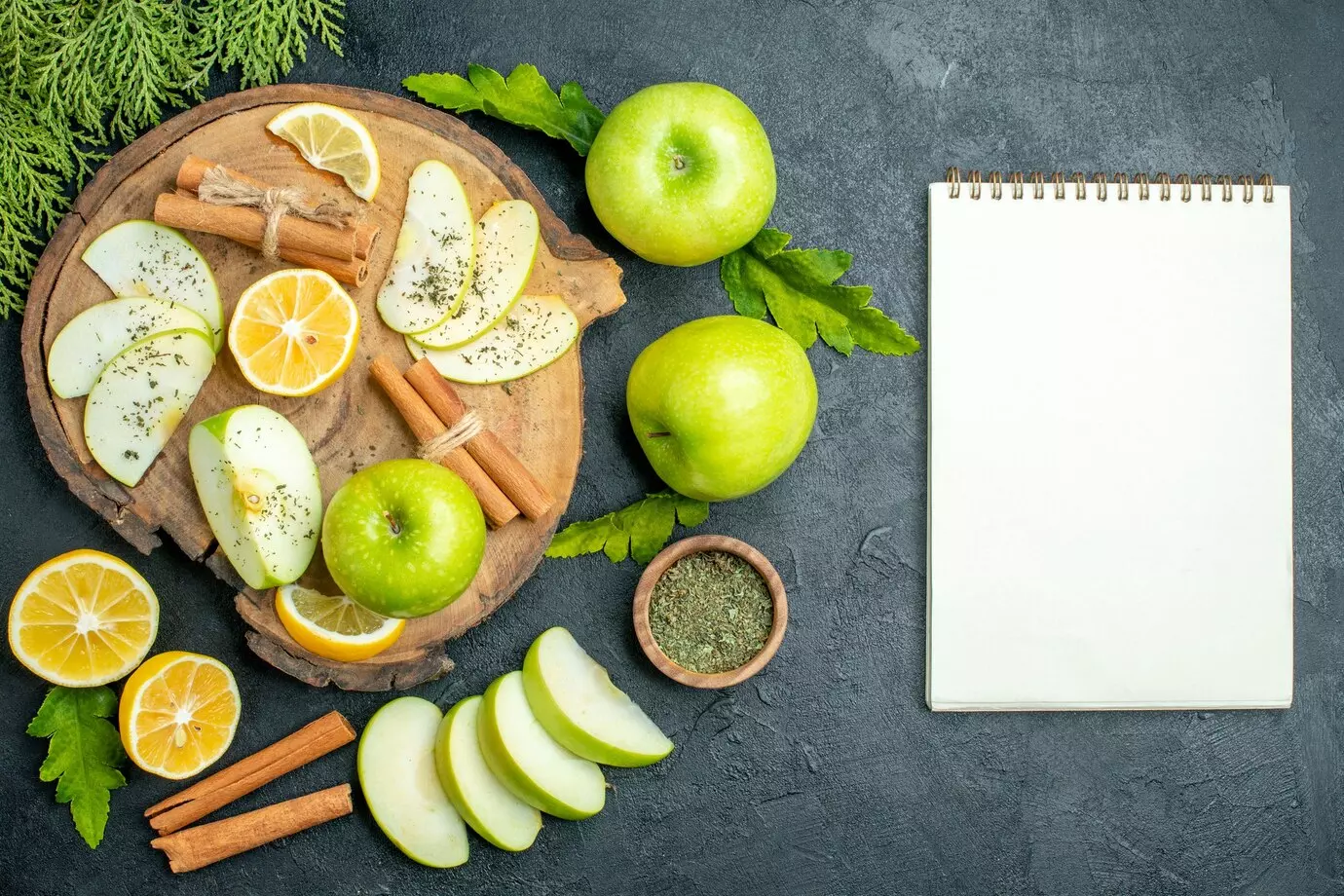 top-view-green-apples-cinnamon-sticks-lemon-slices-apple-slices-wood-board-cut-lemons-apples-notebook-black-table_140725-145476